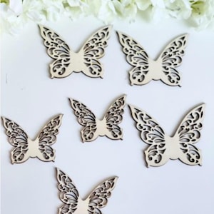 Op de afbeelding: Zes houten vlinderuitsnijdingen met ingewikkelde ontwerpen. De vlinders zijn in een halve cirkel op een witte achtergrond gerangschikt.