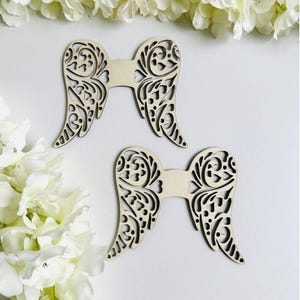 May include: Two pairs of wooden angel wings with intricate cut-out designs. The wings are made of light brown wood and have a delicate, lacy appearance.
