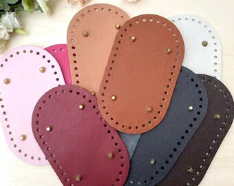 Op de afbeelding: Een collectie ovale tassentassen in diverse kleuren, waaronder roze, magenta, beige, bruin, wit, donkergrijs en donkerbruin. Elke basis heeft een getextureerd oppervlak, een rand met voorgeponste stikgaatjes en vier kleine metalen voetjes.