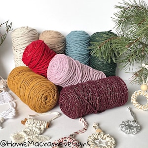 Op de afbeelding: Assortiment van acht spoelen macramékoord in verschillende kleuren, waaronder rood, mosterdgeel, roze, teal, groen en bordeauxrood. De koorden hebben een subtiele glans en zijn gerangschikt op een wit oppervlak met decoratieve items.