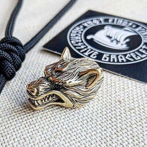 May include: A detailed brass wolf head charm with a snarling expression. The charm is a detailed, realistic depiction of a wolf's head with a textured surface. The charm is a popular choice for jewelry making and is often used to create necklaces, bracelets, and keychains.