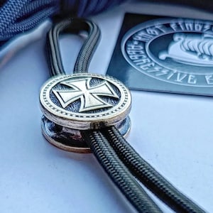 May include: A black paracord lanyard with a brass toggle featuring a silver iron cross design.
