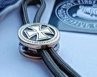 May include: A black paracord lanyard with a brass toggle featuring a silver iron cross design.