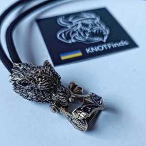 Peut inclure: Un pendentif en bronze représentant une tête de loup détaillée, avec un cordon noir. La tête de loup est sculptée avec soin et présente une finition texturée. Le pendentif est attaché à un cordon noir avec un fermoir en métal.