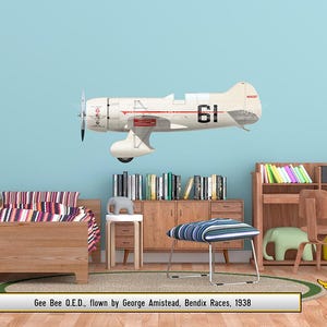 Könnte beinhalten: Ein cremefarbenes Gee Bee O.E.D. Flugzeug mit der Nummer 61, roten Akzenten und einem Propeller ist an einer hellblauen Wand angebracht. Der Raum verfügt über Holzmöbel, ein Bett, einen Schreibtisch und einen gestreiften Hocker. Das Bild ist 152 cm groß.