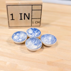 Puede incluir: Cuatro pequeños cuencos de cerámica blanca con un patrón de burbujas azul y blanco. Los cuencos tienen un diámetro de aproximadamente 2,5 cm.
