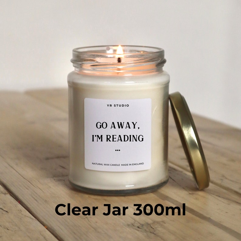 May include: A clear glass jar candle with a gold lid. The candle is lit and the label reads "YR STUDIO, GO AWAY, I'M READING... NATURAL WAX CANDLE MADE IN ENGLAND". The jar is 300 ml.