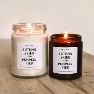 K&ouml;nnte beinhalten: Zwei Kerzen in Bernstein- und Klarglasbeh&auml;ltern. Beide Kerzen haben wei&szlig;e Etiketten mit schwarzem Text, der "YR Studio, Autumn Skies and Pumpkin Pies, Natural Wax Candle Made in England" lautet.