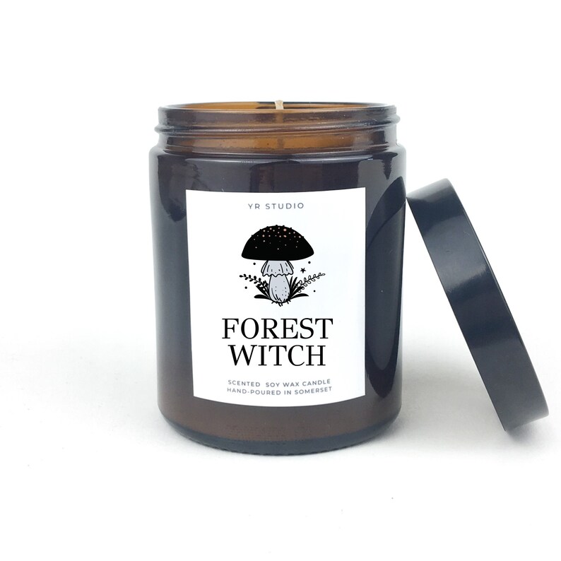 May include: A brown glass jar candle with a black lid. The label reads "YR STUDIO" and "FOREST WITCH" with a mushroom illustration. The candle is scented soy wax and hand-poured in Somerset.