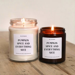 May include: Two glass candle jars with brown lids. Both candles are lit and have white labels with black text that reads "YR Studio Pumpkin Spice and Everything Nice" and "Natural Wax Candle Made in England".