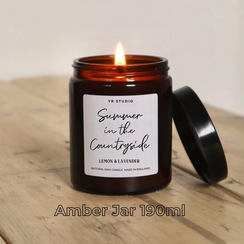 May include: Amber glass candle jar with a black lid. The candle is lit and the label reads "YR STUDIO Summer in the Countryside Lemon & Lavender Natural Wax Candle Made in England".