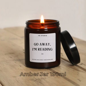 May include: Amber glass candle jar with a black lid. The candle is lit and the label reads "Go Away, I'm Reading..."  Natural Wax Candle Made in England. The jar is 190 ml.
