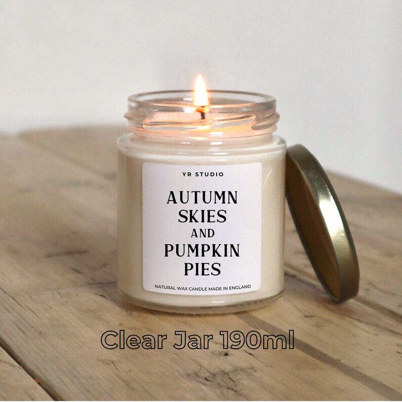 K&ouml;nnte beinhalten: Eine Kerze in einem durchsichtigen Glasgef&auml;&szlig; mit goldenem Deckel. Die Kerze ist mit "YR STUDIO Autumn Skies and Pumpkin Pies Natural Wax Candle Made in England" beschriftet. Die Kerze ist angez&uuml;ndet und die Flamme ist sichtbar. Das Gef&auml;&szlig; hat ein Fassungsverm&ouml;gen von 190 ml.
