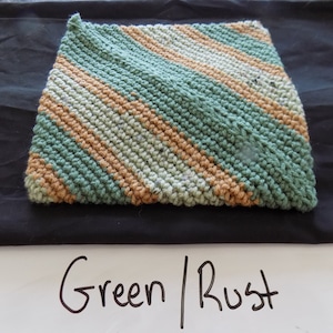 May include: A knitted dishcloth with diagonal stripes in green, beige, and rust colors. The text "Green/Rust" is written below the dishcloth.