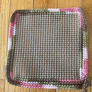 May include: A beige crochet canvas with a brown, pink, and green border. The canvas is made of plastic mesh and is ready for needlepoint or cross-stitch.