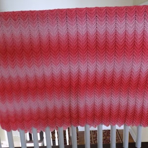 May include: A pink and white ombre crochet blanket with a chevron pattern. The blanket is hanging on a white railing.