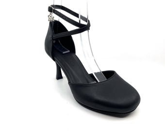 May include: Black leather heeled shoes with an ankle strap and a small decorative charm.