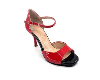 May include: Red and black open-toe heeled dance shoes with an ankle strap and a small charm. The shoes have a black heel and a black toe.
