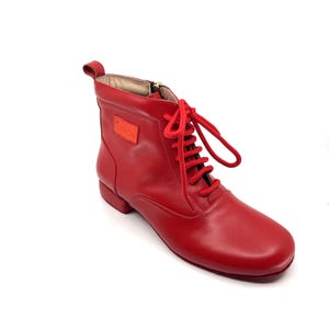 以下が含まれることがあります： レースアップとサイドジッパーが付いた赤い革製のアンクルブーツ。ブーツはローヒールで丸みを帯びたつま先です。