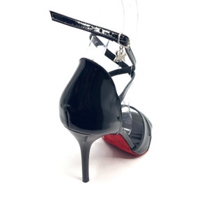 May include: Black leather heeled sandals with a red sole and a silver charm on the ankle strap.