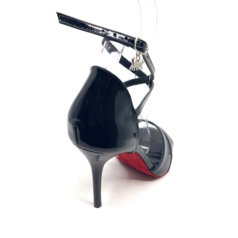 May include: Black leather heeled sandals with a red sole and a silver charm on the ankle strap.