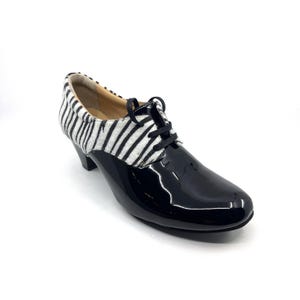 Könnte beinhalten: Schwarzer Lackleder-Oxford-Schuh mit Zebra-Print-Akzent am Obermaterial. Der Schuh hat einen kleinen Absatz und schwarze Schnürsenkel. Geeignet für formelle oder elegante Anlässe.