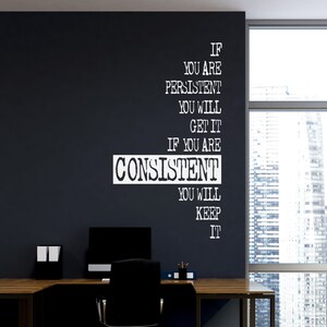 Puede incluir: Una cita motivacional en texto blanco sobre una pared oscura. La cita dice: "Si eres persistente, lo conseguirás. Si eres constante, lo mantendrás". Un escritorio y una silla de oficina están en primer plano.
