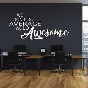 May include: A motivational quote on a dark gray wall in a modern office setting. The quote reads "We don't do average, we do awesome". The office has two desks with black chairs and a large window with a city view.