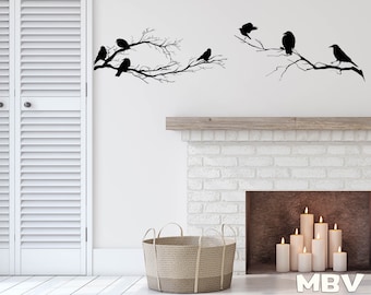May include: Black silhouette wall decal of a flock of birds perched on bare branches. The decal is displayed on a white wall above a white brick fireplace with candles inside.