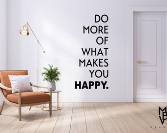 May include: A motivational quote, "Do more of what makes you happy." is displayed on a white wall in a living room setting. A brown armchair with a white pillow is in the foreground, and a potted plant is on a side table.