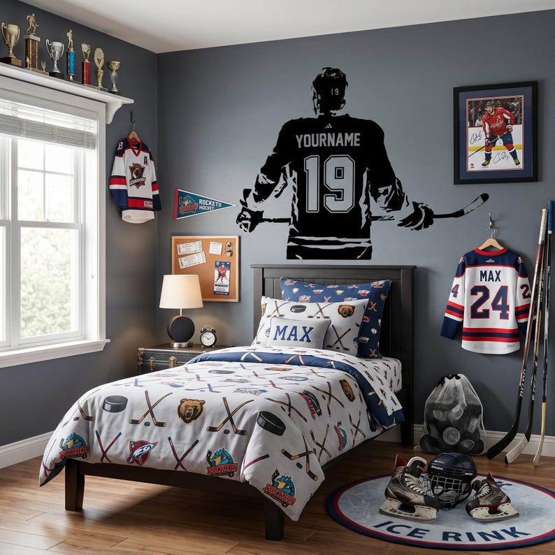 May include: A bedroom featuring a wall decal of a hockey player with the text YOURNAME and 19, a bed with hockey-themed bedding, two hockey jerseys with the names MAX and 24, hockey sticks, skates, and a round rug with the text ICE RINK.