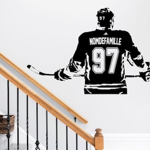 May include: A black wall decal depicting a hockey player from behind, wearing a jersey with the number 97 and the text NOMDEFAMILLE. The player holds a hockey stick horizontally across their back, with the number 97 also visible on the helmet.