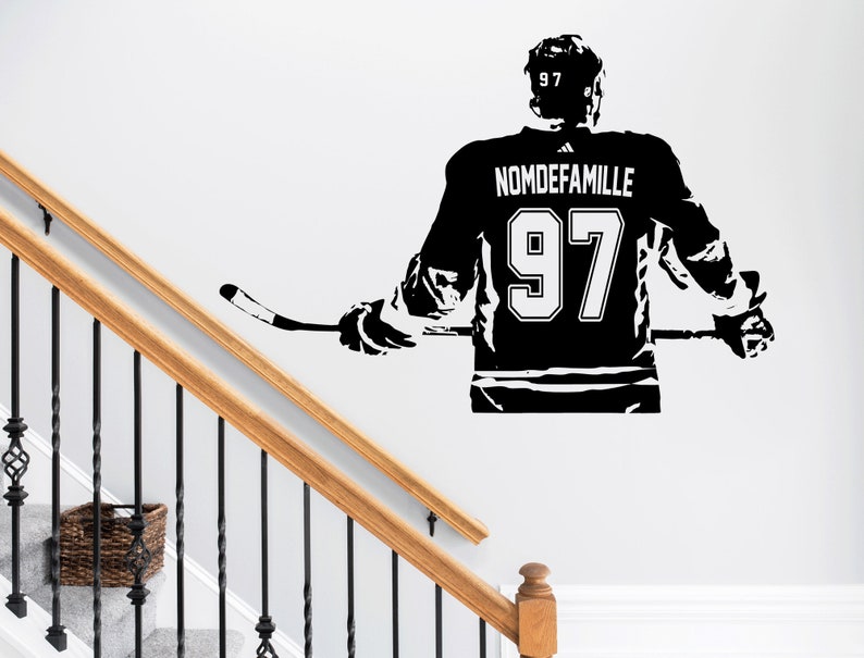 May include: A black wall decal depicting a hockey player from behind, wearing a jersey with the number 97 and the text NOMDEFAMILLE. The player holds a hockey stick horizontally across their back, with the number 97 also visible on the helmet.
