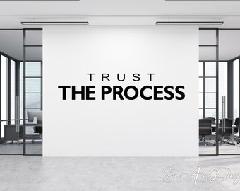 May include: A white wall with the text "TRUST THE PROCESS" in black letters. The wall is in a modern office setting with glass walls and a conference table with chairs.
