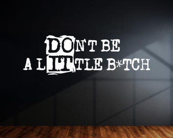 Puede incluir: Texto blanco sobre una pared negra que dice "DON'T BE A LITTLE B*TCH" en una fuente audaz y desgastada. La pared tiene un acabado liso y oscuro, y el suelo es de tablones de madera.