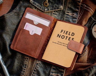 May include: A brown leather notebook cover with a pocket for cards and a Field Notes notebook inside. The notebook cover has a flap that closes with a snap.