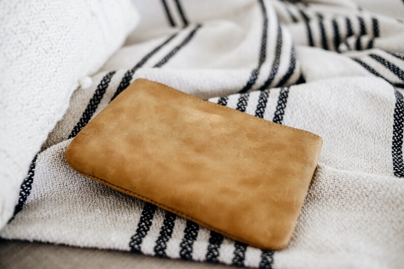 May include: A brown suede clutch purse on a white and black striped throw blanket.