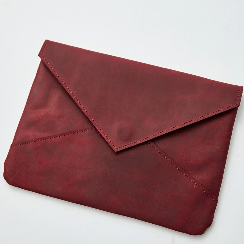 May include: A burgundy leather clutch with a flap closure. The clutch has a simple, elegant design.