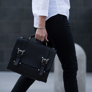 May include: A black leather satchel with silver buckles and metal accents. The bag has a flap closure and a top handle.