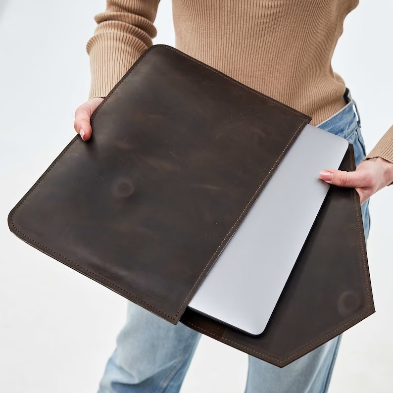 Puede incluir: Una funda para port&aacute;til de cuero marr&oacute;n con un ordenador port&aacute;til en su interior. La funda tiene una solapa que se cierra con un cierre magn&eacute;tico.