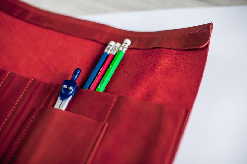 K&ouml;nnte beinhalten: Ein rotes Leder-Bleistift-Etui mit vier Bleistiften und einem Zirkel. Die Bleistifte sind blau, rot, gr&uuml;n und wei&szlig;.