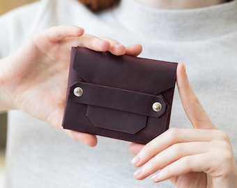 May include: A burgundy leather wallet with a flap closure and two silver snaps. The wallet is held in a person's hands.