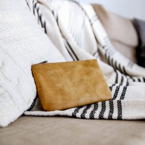 May include: A tan leather zippered pouch resting on a white and black striped throw blanket on a couch.