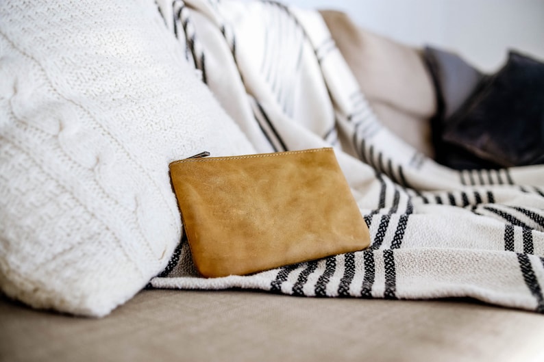 May include: A tan leather zippered pouch resting on a white and black striped throw blanket on a couch.