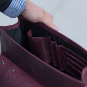 May include: A burgundy leather briefcase with multiple interior pockets and a flap closure. The briefcase is open and the interior is visible.