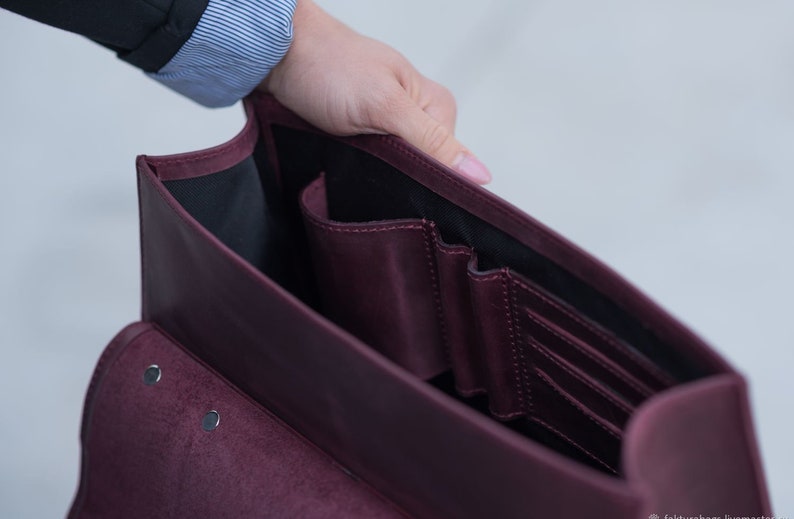 May include: A burgundy leather briefcase with multiple interior pockets and a flap closure. The briefcase is open and the interior is visible.