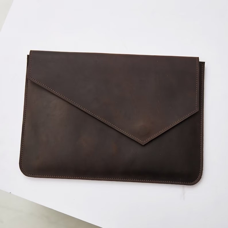 Puede incluir: Una funda para port&aacute;til de cuero marr&oacute;n con cierre de solapa. La funda tiene un aspecto desgastado sutil y est&aacute; cosida con un hilo contrastante.