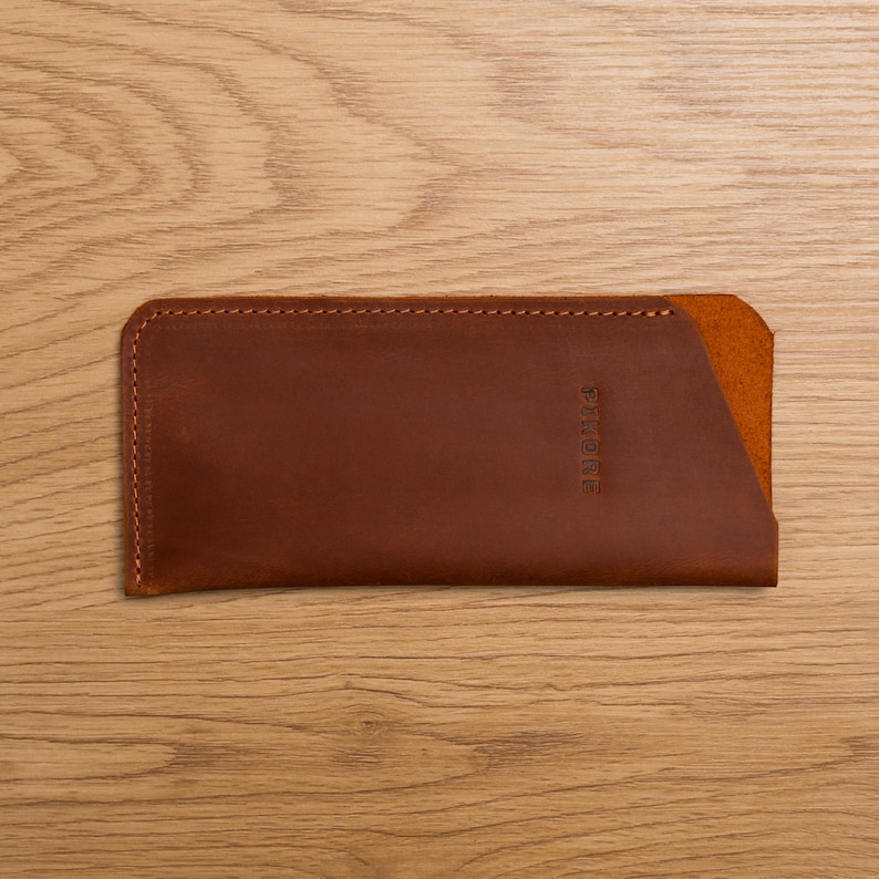 May include: A brown leather phone case with a stitched edge and the word "STOWRE" embossed on the front.