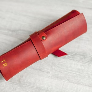 K&ouml;nnte beinhalten: Eine rote Lederrolle mit einem goldenen, gepr&auml;gten Monogramm "TR".