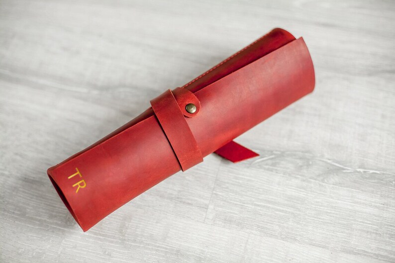 K&ouml;nnte beinhalten: Eine rote Lederrolle mit einem goldenen, gepr&auml;gten Monogramm "TR".